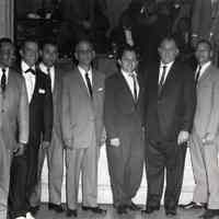 B+W group photo of eight men posed in front of a stage, (Hoboken), no date, ca. 1960-1970.