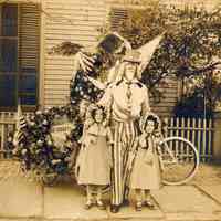 Sepia-tone photo of a person in Uncle Sam costume with two costumed girls, no place, no date, ca. 1912-1925.