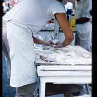 Color slide of a man make food at a street fair.