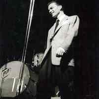 Black-and-white photo of a young Frank Sinatra onstage with Tommy Dorsey Band, no place, no date, ca. 1940-42.