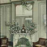 Lantern slide, color, of a room with floral arrangements on a mantle, used for promotional display in Hoboken, no date, ca. 1920.