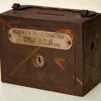 Steel bank with handle and coin slot with a plate that reads " Hoboken Trust Company, Hoboken, N.J., corner Washington and 14th Streets."-