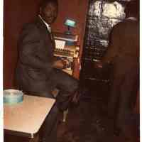 Digital copy of color photo of Charles McNeil seated at the a cash register, Zanzibar Club, Hoboken, circa late 1960