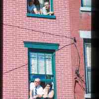 Color slide of people looking out of the windows of a brick building.