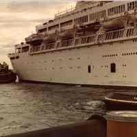 Digital scan of color photo of a passenger vessel with tugboat, location not given, no date, circa 1970-1980.