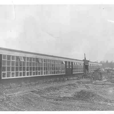 Side view of Lakeview school with various construction equpiment in front of the far end of the building and a man standing in what appears to be a doorway
