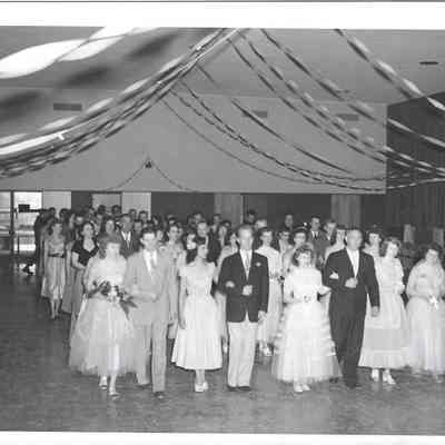 Several rows of young women and adult men lined up on dance floor under streamers, some girls uncoupled