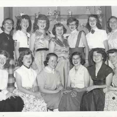Thirteen young pageant contestants in two rows in front of inset display case