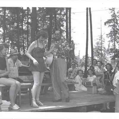 Emcee Larry Kirkwood hands microphone to pageant queen Audrey Moe on stage with princess Yvonne Knotek