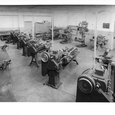 Machine workshop with two rows of machines and a wrap around workbench in a room painted with a lifght upper half and dark bottom half