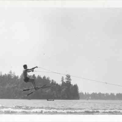 Man water skiing, mid-air, boat visible in background