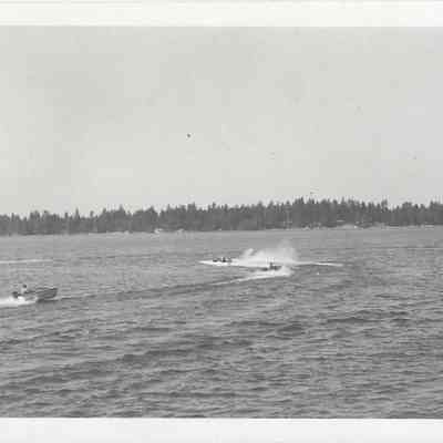 Four boats leading water skiers on lake, tree-covered shore off in the distance