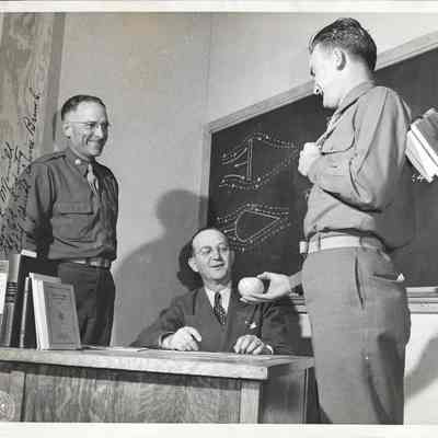 A. G. Hudtloff receives apple from student in front of Colonel Alive Merrill