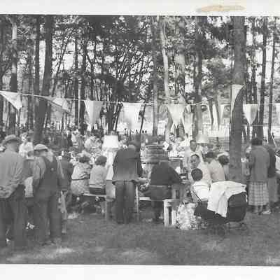 People in a tree covered area sitting at tables and playing bingo