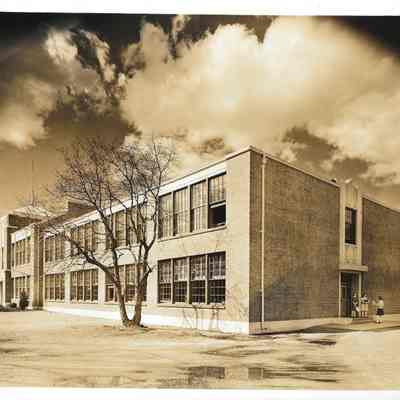Right side street view of Clover Park High School with several young women standing in front of the side entrance and clouds billowing overhead
