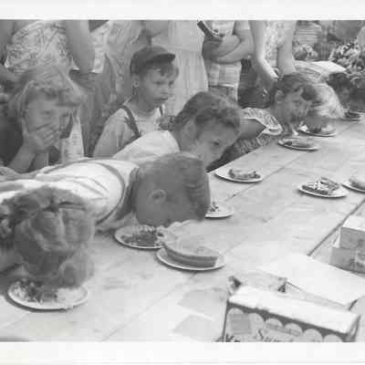 Children participating in a pie eating contest in front of closely packed crowd