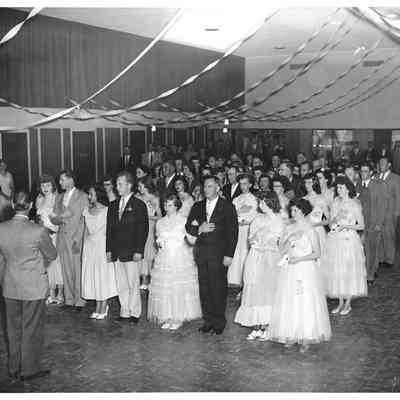 Adult men and young women arm and arm under a ceiling full of streamers