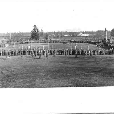 Wide shot of people standing around foot ball field saluting