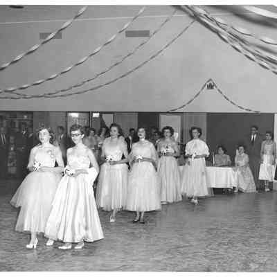 Six young women in pairs of two holding small bouquets beneath streamers