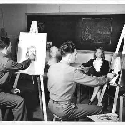 Two mnilitary men in uniform painting picture of female model in front of chalkboard
