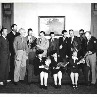 14 people on and around couch looking at objects made at Hobby House