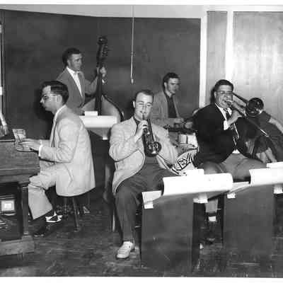 Five members of band playing instruments in front of podiums