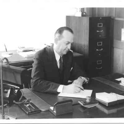A. G. Hudtloff writing diligently while sitting at desk in office