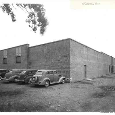 Brick vocational shop with several cars parked on the side and shadow of a person on the right