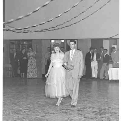 Lone man and young woman arm in arm under streamers at pageant comeptition