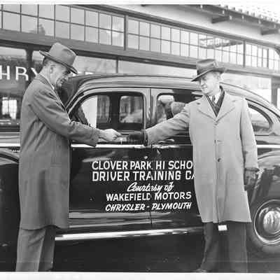 A. G. Hudtloff receiving keys from another man while standing in front of a car with Clover Park Hi School Driver Trianing Car printed on it