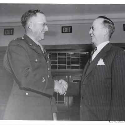 Closeup of Col. Alvie Merrill gleefully shaking hands with A. G. Hudtloff.