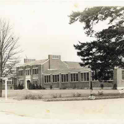 Front view of unnamed brick building with several trees and a sign pointing to lakeview Cloverpark and Tacoma in front