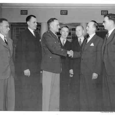 Wide shot of A. G. Hudtloff shaking hands with Col. Alvie Merrill in front of five other men