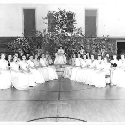 Copy of four rows of girls in white sitting in a v-formation in front of three other girls on a podium