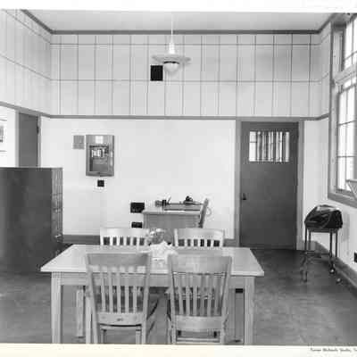 Partially tiled empty room with one open window, two tables, one with four chairs and a small elephant vase