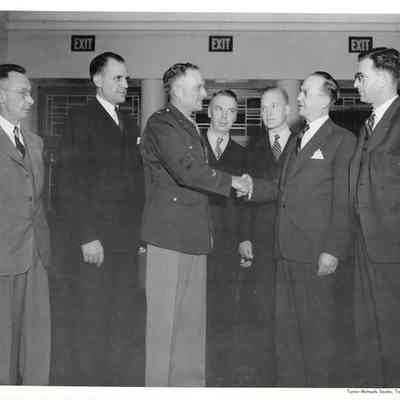 Shot of A. G. Hudtloff shaking hands with Col. Alvie Merrill in front of five other men in Clover Park lobby