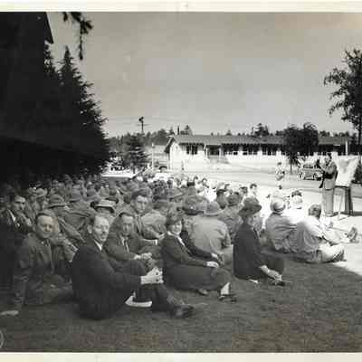People sitting on grass watching Dr. Marvin Schaffer give orientation lecture