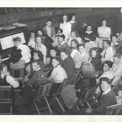 Group of teenagers sat in circle around boy playing the piano