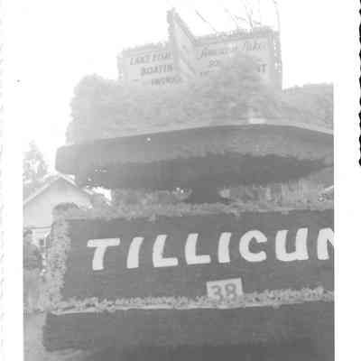 Rear view of the 3/4 view of the Front view of the American Lake Improvement Club/Tillicum float for Daffodil Parade, building and people visible in middle left