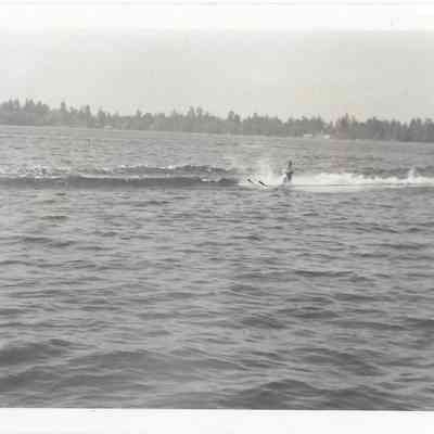 Young man water skiing on lake, treeline in distance