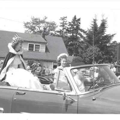 Queen Audrey Moe riding in back of convertible with young girl and Bob Miller as chauffer