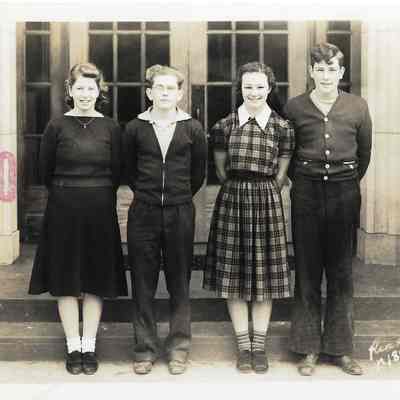 Four young people in front of building with their arms held behind their backs