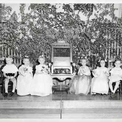 Six Young children dressed for special occasion and sitting on a platform on either side of a large chair/throne