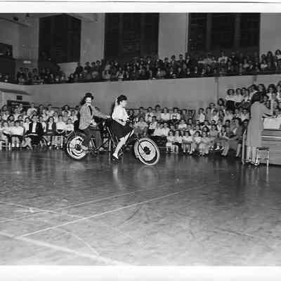 Couple riding tandem bike in front of gym assembly