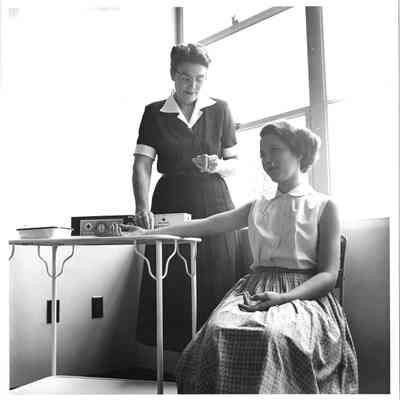 Teenager getting pulse taken by adult woman at Hudtloff Junior High 1953