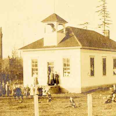 A photo of a schoolhouse and schoolyard, with many schoolchildren gathered in front of the building: 2023_001_I_F_a03