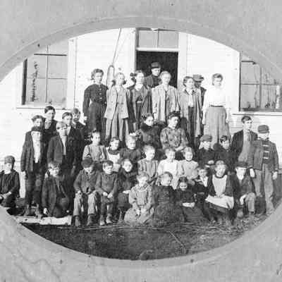 Black and white photograph of schoolchildren gathered on the front steps of a schoolhouse: 2023_001_I_F_a02