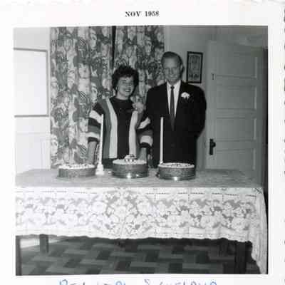 Rev + Mrs Sigueland, Nov 1958: A black and white photograph of a couple standing behind a table with a trio of cakes. 2023.001.V.010