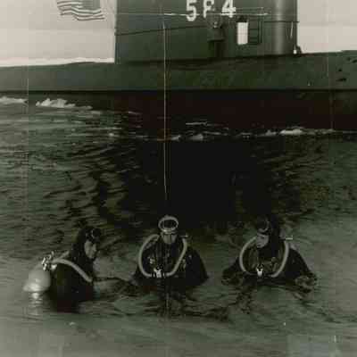 Three U.S. Navy divers outside of a submarine.
