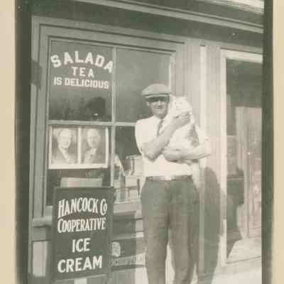 Byron (Bide) Moore with a cat in front of the Moore Brothers' Store in Prospect Harbor